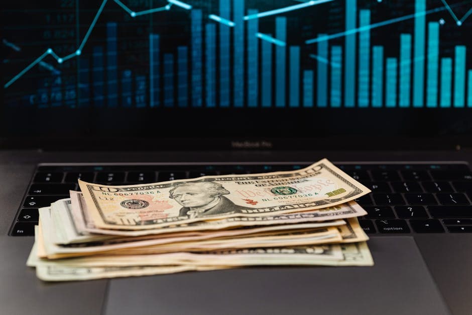 US dollar bills on laptop with financial graph in background, symbolizing wealth and technology.